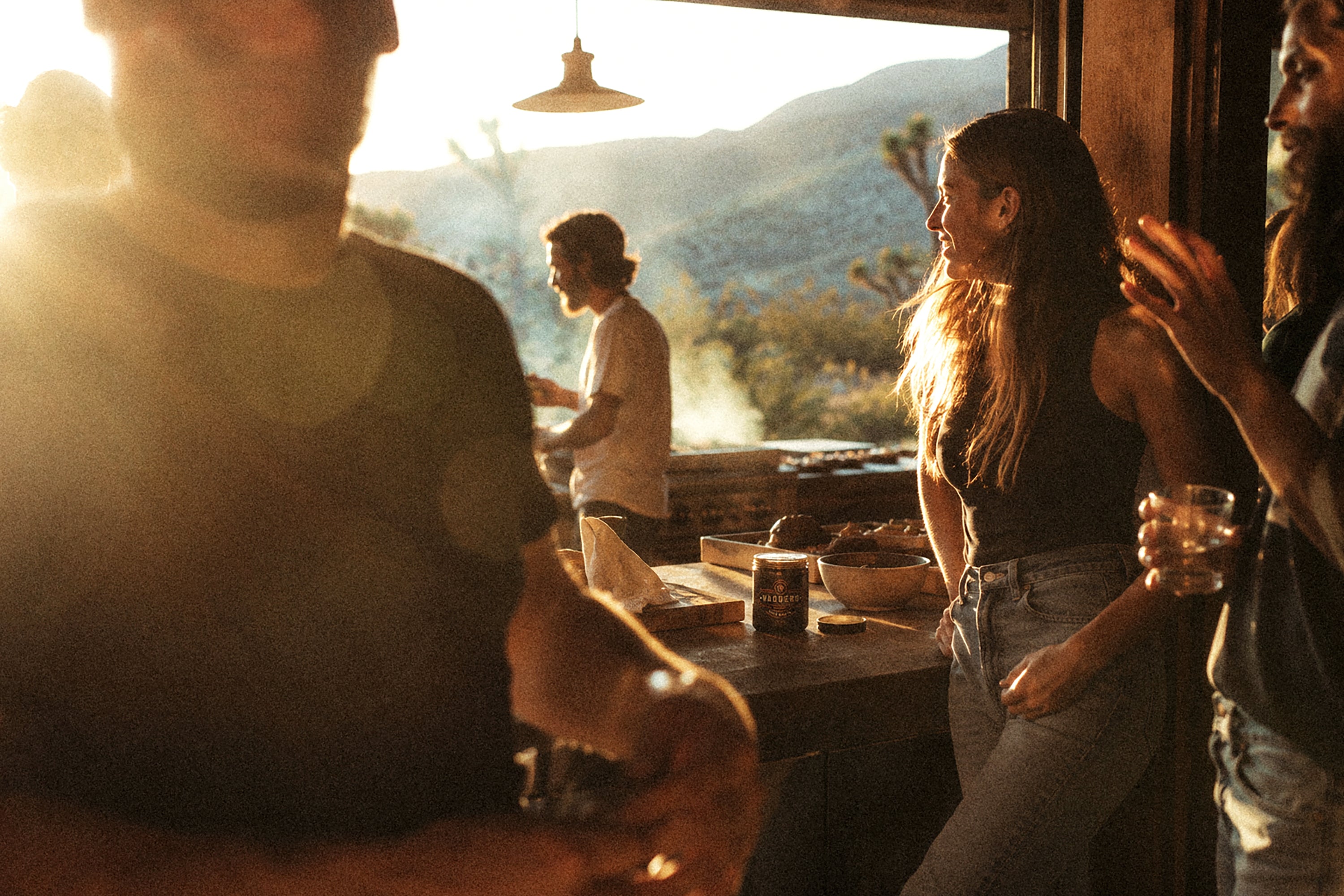 Friends gathering around food in a sunlit kitchen