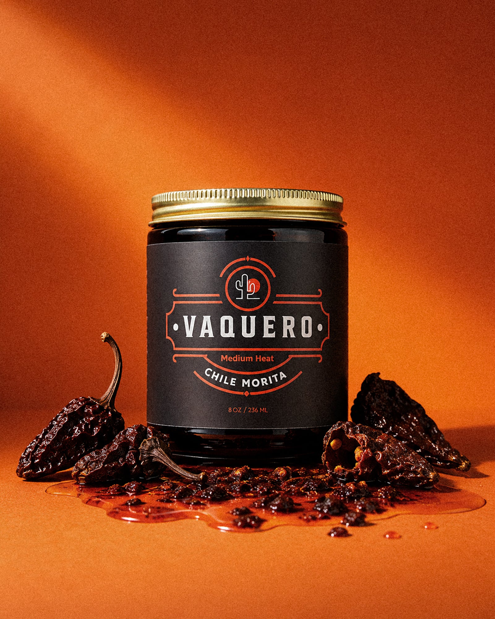 Vaquero Chile Morita jar with morita chiles on an orange backdrop